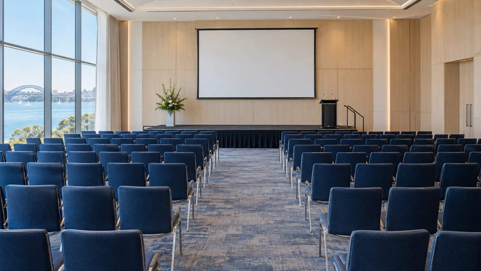 Illustrative conference hall with rows of blue chairs facing a presentation screen and lectern